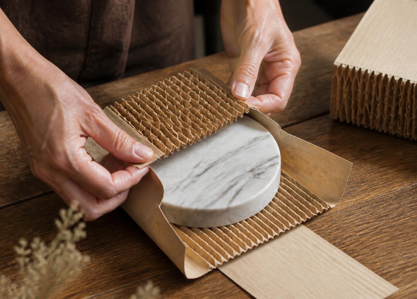 Hands wrapping a marble homeware piece in honeycomb kraft cardboard
